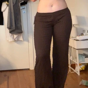 Bruna vida byxor med struktur - Säljer ett par bruna byxor med lätt strukturerat tyg och vida ben. Byxorna har en enkel design utan synliga detaljer som dragkedja eller knappar och sitter bekvämt i midjan. Perfekta för en avslappnad och trendig look.