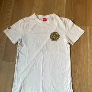 Vit t-shirt från Santa Cruz med leopard mönster - Vit t-shirt från Santa Cruz med tryck i leopardmönster och japansk text både fram och stort bak. Klassisk passform och korta ärmar. Perfekt för dig som gillar streetwear och snygga detaljer. Har aldrig använt den då jag köpte den och glömde bort att den jag hade den.