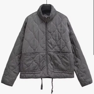 Grå quiltad jacka från Zara - Quiltad jacka från Zara i grått med snyggt vågigt mönster. Jackan har dragkedja framtill, två stora fickor och snörning i nederkant. Perfekt för lager-på-lager och chill höst- eller vårstil. Materialet är mjukt och känns skönt mot huden.