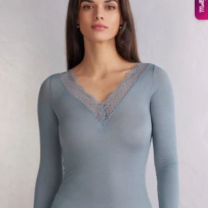 Ljusblå långärmad topp med spets - Supersnygg ljusblå långärmad topp med djup v-ringning och spetsdetalj längs halsringningen. Tight passform som framhäver figuren och ger en stilren look. Perfekt att styla med jeans eller kjol för en trendig vibe. Använd ungefär 3 gånger.