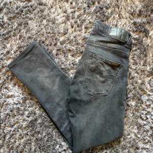 Svarta Nudie grim tim  - Snygga svarta jeans från Nudie Jeans med klassisk femficksdesign och diskret logga på bakfickan. Jeansen har en smal passform och raka ben, tillverkade i mjukt bomullstyg med lite stretch för extra komfort. Jeansen köpta för 1600kr på jeansbolaget och de är i storlek 28/32 men har kortat ner de så de är som 28/30. Jeansen är lite små på mig och är 177 cm skulle nog passa någon som är under 174cm och under. Jeansen är i väldigt bra skick och är sparsamt använda, finns inga hål. Perfekt för hösten