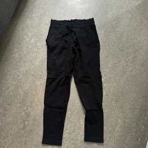 Svarta mjukisbyxor från ONLY  - Svarta mjukisbyxor från ONLY med elastisk midja och snörning. Byxorna har raka ben, fickor fram och bak samt en bekväm passform. Perfekta för chill dagar eller när du vill ha något skönt på dig. Storlek XS.