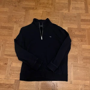 Mörkblå half zip tröja från Lexington - Mörkblå långärmad tröja från Lexington med stilren half zip-dragkedja och liten logga på bröstet. Tröjan har hög krage och är gjord i mjuk bomull. Andvänd 5-6 gånger