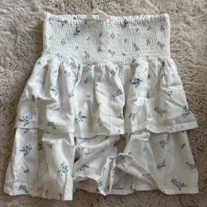 Vit blommig volangkjol med smock - Supersöt kort kjol i vitt med små blå blommor och volanger. ‼️Aldrig använd‼️Strl 170 & kommer från H&M. 🩷
