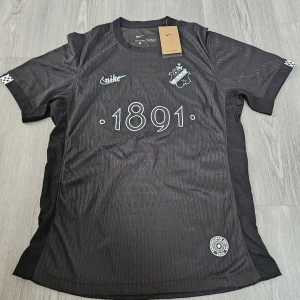AIK x Nike svart fotbollströja 2025 - AIK Smokinglirare Edition 2025 fotbollströja i svart med diskreta ränder, broderat klubbmärke och Nike-logga på bröstet. Siffran 1891 tryckt framtill. Tillverkad i lätt och ventilerande Dri-FIT-material. Kortärmad modell med rund hals.