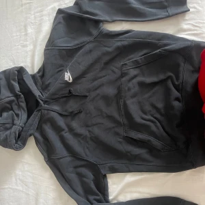 Svart Nike hoodie med huva och ficka - Svart hoodie från Nike i storlek S med klassisk logga broderad i vitt på bröstet. Tröjan har huva med snörning och en stor magficka framtill. Mjuk bomullskänsla och långärmad modell, perfekt för chill eller streetwear.
