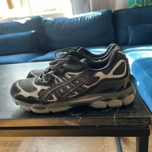 Svarta och grå Asics sneakers - Svarta och grå sneakers från Asics med meshpaneler och detaljer i syntet. Skorna har snörning och en robust, dämpad sula som passar perfekt för långa promenader eller träning. Klassisk sportig look med Asics-logga på sidan. Köpta begagnat helt nya och sedan använt de 1 gång och lagt bort de. Som nya utöver lite damm på mockan då de har legat i en skobox ett tag och lite smuts på sulan från den gången jag använde de. Kan möjligen sänka priset lite om snabb affär. Storlek 44 