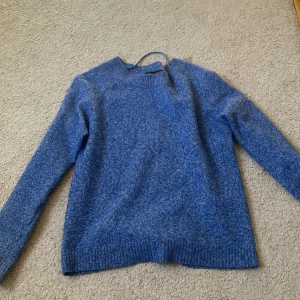 Blå stickad tröja med rund hals - Mysig blå stickad tröja med rund hals och långa ärmar. Tröjan har en enkel och stilren design med ribbade muddar vid ärmslut och nederkant. Perfekt för lager-på-lager under kyliga dagar. Priset kan diskuteras 