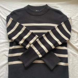 Svart och vit randig stickad tröja XS - Snygg stickad tröja från Gina Tricot i svart med vita horisontella ränder. Modellen har rund hals, långa ärmar och breda ribbade muddar vid ärmslut och nederkant. Perfekt för dig som gillar klassisk stil med en twist.