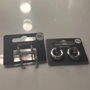 Två par silvriga örhängen Montini - Säljer två par snygga örhängen från Montini. Ena paret är små hoops med glittriga stenar, det andra är chunky ringar med textur. Perfekt för att lyfta din stil med lite extra bling. Båda är i silverfärg och passar till många looks.