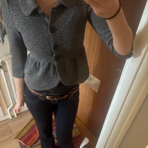 Grå kavaj med trekvartsärm - Snygg grå kavaj med trekvartsärmar och markerad midja. Jackan har stora knappar framtill och ett klassiskt krage. Perfekt för dig som vill ha en stilren och tidlös look.