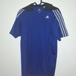 Blå Adidas fotbollströja S - Snygg blå fotbollströja från Adidas med klassiska vita ränder på axlarna och svart mesh vid axelpartiet. Tillverkad i lätt och ventilerande polyester med ClimaCool-teknologi. Perfekt för träning eller match, med rund hals och korta ärmar.