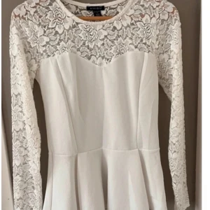 Vit spetstopp från Amisu - Supersöt  från Amisu med långärmade spetsdetaljer och blommigt mönster upptill. har rund halsringning och en feminin, figursydd med volang ner till