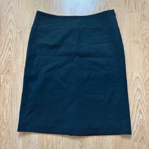 Svart klassisk pennkjol från Mexx - En stilren svart pennkjol med enkel design och rak passform. Kjolen är knälång och har en diskret dragkedja i sidan. Perfekt för dig som gillar minimalistisk stil och vill ha en kjol som funkar till många olika looks