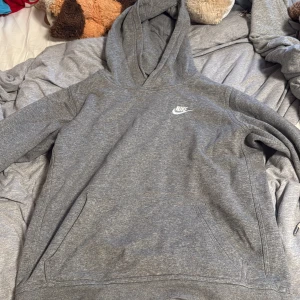 Grå hoodie från Nike S - Säljer en grå Nike hoodie i storlek S med klassisk logga på bröstet. Tröjan har huva, känguruficka och långa ärmar. Perfekt för chill dagar eller när du vill ha en enkel och snygg look. Materialet är mjukt och skönt, troligtvis bomull och polyester. Står xl men passar S