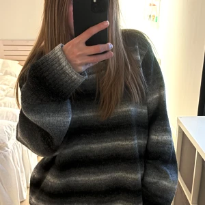Grå stickad tröja  - Mysig stickad tröja med breda ränder i olika grå nyanser. Modellen är oversized med långa ärmar och ribbade muddar.