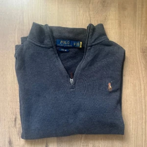 Ralph Lauren half zip - Snygg mörkgrå tröja från Polo Ralph Lauren i storlek XS. Tröjan har half zip och klassisk broderad logga på bröstet. Materialet är ribbad bomull som känns mjuk och skön mot huden. Perfekt för dig som gillar stilrena och tidlösa plagg.
