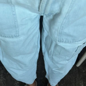 Ljusblå cargopants i jeansmaterial - Säljer ett par ljusblå cargopants i jeansmaterial med raka ben och stora fickor på sidorna. Byxorna har croppad längd och avslappnad passform, perfekta för en chill och trendig look.