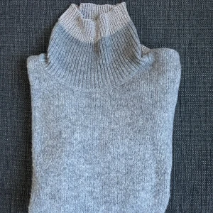Grå polotröja i ullmix - Mysig grå polotröja med ribbad hög krage och muddar i ljusare grå ton. Tröjan är stickad och har lång ärm, perfekt för kyliga dagar. Enkel och stilren design som funkar till allt. Materialet känns mjukt och värmande.