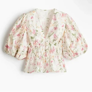 Blommig blus med puffärm och v-ringning - Supersöt blommig blus med v-ringning och voluminösa puffärmar. Den har smockad midja som ger en snygg siluett och är perfekt för dig som gillar romantisk stil. Ljus botten med rosa och gröna blommor. Perfekt till jeans eller kjol!