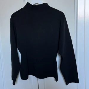 Svart polotröja från Stockh LM Studio - Svart polotröja från Stockh LM Studio i storlek XS. Tröjan har lång ärm och en högre krage som ger en clean och stilren look. Perfekt att matcha med jeans eller kjol för en enkel men snygg outfit.