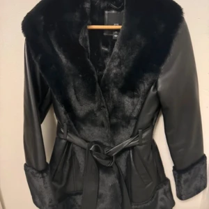 Svart pälsjacka med bälte - Snygg svart pälsjacka från river Island  med fejkpäls på krage
