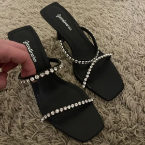 Svarta Stradivarius sandaler  - Svarta sandaler från Stradivarius med fyrkantig tå och två remmar täckta av glittrande strass.  Storlek 37