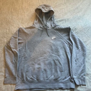 Grå Nike hoodie - Säljer en klassisk grå hoodie från Nike med vit logga på bröstet. Perfekt för chill dagar eller när du vill ha en enkel och stilren look. Vid snabb affär kan priset diskuteras!