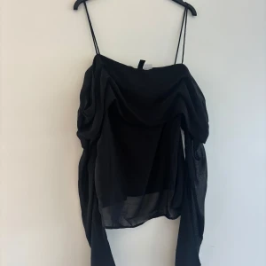 Svart offshoulder topp från Divided - Säljer en svart offshoulder topp från Divided med tunna axelband och draperad chiffongliknande tyg. Aldrig använd.