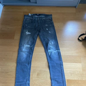 Replay jeans med slitningar - Säljer ett par gråa  jeans från Replay med slitna detaljer och hål på knäna. Jeansen har klassisk femficksdesign, låg midja och är tillverkade i stretchig bomullsdenim för en tight passform. Perfekta för en avslappnad och edgy stil. W30 L34. Skriv om ni undrar något, pris kan diskuteras vid snabb affär. 