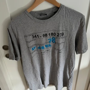 Diesel tshirt - Svin snygg grå t-shirt från Diesel med coolt svart och blått tryck framtill. Mjuk och skön i bomull, perfekt för en chill och avslappnad stil. 