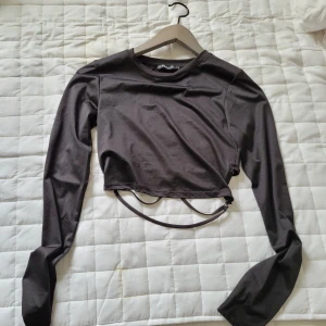 Långärmad festtopp - Snygg svart croppad långärmad topp med unika snörningsdetaljer och ringar nedtill. Toppens material är stretchigt. och 