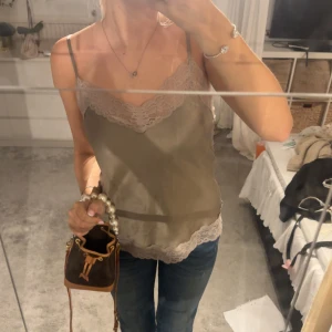 Beige satinlinne med spetskant - Supersnyggt beige linne i satin med tunna axelband och v-ringning. Toppen har fina spetsdetaljer längs urringning och nederkanten, banden är reglerbara🥰