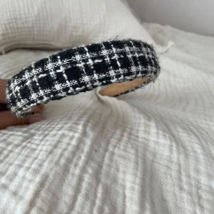 Svartvitt rutigt diadem i ullmix - Trendigt diadem med svartvitt rutigt mönster och bred modell. Ytan är i en grovstickad ullmix.