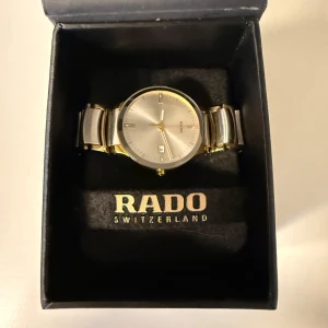 Rado Centrix silver/guld herrklocka - Stilren Rado Centrix herrklocka med rund urtavla i silver och datumvisning. Armbandet är i kombinerat silver- och guldfärgat metall, vilket ger en lyxig känsla. Klockan är Swiss Made och vattentålig upp till 30 meter. Perfekt accessoar för dig som gillar klassisk design.