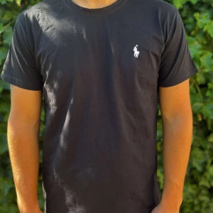 Svart t-shirt från Polo Ralph Lauren - Svart t-shirt från Polo Ralph Lauren med klassisk rund hals och korta ärmar. T-shirten har en vit broderad Polo-logga på bröstet och är gjord i mjuk bomull. Passformen är normal och stilen är clean och enkel, perfekt till jeans eller shorts.                                                                                                                                                                   Nypris:699kr GORILLAPRIS:349kr              Skick: 10/10 Oöppnad                KVITTO MEDKOMMER