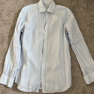 Ljusblå linneskjorta från Massimo Dutti - Säljer en stilren ljusblå skjorta från Massimo Dutti i 100% linne. Skjortan är i grymt skick och använd fåtal gånger säljer pga för liten på mig, perfekt under en Stickad tröja.