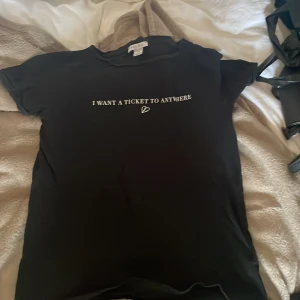 Svart t-shirt med text från Amisu - Svart t-shirt från Amisu i storlek XS med vit text på bröstet: 'I WANT A TICKET TO ANYWHERE' och ett litet hjärta under. Klassisk rund halsringning och korta ärmar. Skön och enkel modell som passar till allt.