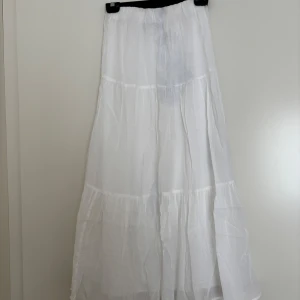 Vit långkjol från Gina Tricot XS - Superfin vit långkjol från Gina Tricot i luftig bomull. Kjolen har flera volanger och resår i midjan för en bekväm passform. Perfekt för varma dagar och ger en riktigt fräsch och somrig vibe. Den har en blåfläck som säkert går att tvätta bort -därav priset. Annars bara använd en gång.