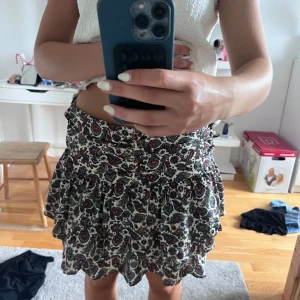 Vit mönstrad volangkjol - Supersöt kort kjol med volanger och paisley-inspirerat mönster i rött, blått, svart och beige på vit botten. Kjolen har bred midja och flowig passform, perfekt till sneakers eller boots. Tyg i mjuk bomullskänsla och riktigt skön att bära.