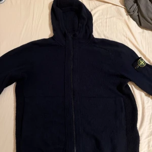 Mörkblå stickad hoodie från Stone Island - Gently used stone island knitted hoodie.  Got receipt. Bought for 6300 SEK in june.  Can send more pictures if interested.  Size M.                                                                                  Säljer en mörkblå stickad hoodie från Stone Island med dragkedja och ikonisk patch på ärmen. Jackan har huva, ribbade detaljer och en clean look som passar perfekt till streetwear. Grym för dig som gillar exklusiva och stilrena tröjor 