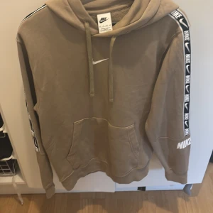 Beige Nike hoodie med logga XS - Köpte till min son men passa inte, nyss köpt på kids brand store för 1199..surt att tappa kvittot.Snygg beige hoodie från Nike i storlek XS. Tröjan har huva med snörning, magficka och svarta band med vita Nike-loggor längs ärmarna. Mjuk bomullskänsla och långärmad modell, perfekt för en chill och sportig look.