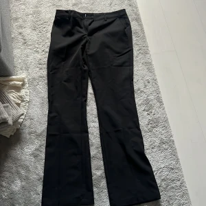 Svarta kostymbyxor från BikBok - Svarta kostymbyxor från BikBok i klassisk modell med raka ben och midja med hällor för bälte. Snyggt skräddade och perfekta till en stilren look. Materialet känns mjukt och har en lätt glansig finish.