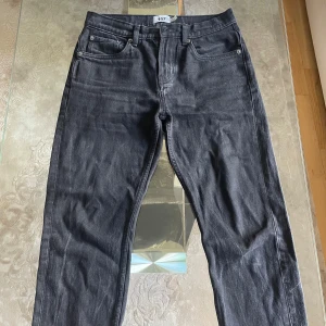 Svarta jeans från 157, straight fit - Svarta jeans från 157 med klassisk femficksmodell och dragkedja. Jeansen har rak passform och är tillverkade i bomullstyg med en snygg mörk tvätt. Perfekta för dig som gillar en enkel och stilren look. Jeansen har vikts vid benen, därför finns det linjer där.
