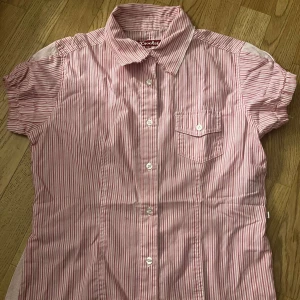 Röd- och vitrandig skjorta från Crocker - Kortärmad skjorta från Crocker i röd- och vitrandigt mönster. Skjortan har klassisk krage, knappstängning framtill och en bröstficka med knapp. 🩷 Använd fåtal gånger. 