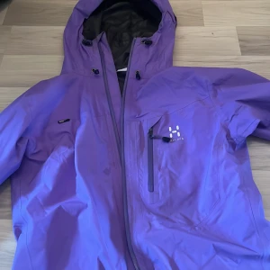 Lila Gore-Tex vindjacka från Haglöfs - Säljer en lila vindjacka från Haglöfs i dammodell, storlek S. Jackan är tillverkad i slitstark Gore-Tex och har huva, dragkedja framtill och praktisk bröstficka. Perfekt för dig som vill ha en snygg och funktionell jacka till utelivet.