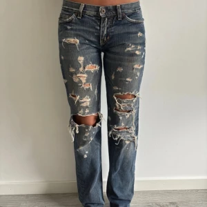 Blå slitna Replay jeans W27 L34 - Säljer ett par blå Replay jeans med rejält slitna och trasiga detaljer över hela benen. Modellen har rak passform och klassisk femficksdesign. Jeansen är i låg midja. 