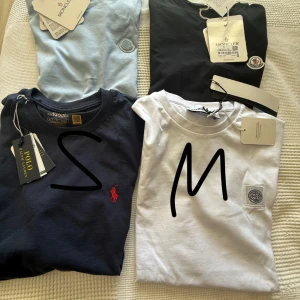 T-shirtpaket Moncler, Stone Island & Polo.  - Fyra snygga t-shirts: ljusblå och svart från Moncler med broderad logga, vit från Stone Island med patch på bröstet och marinblå från Polo Ralph Lauren med röd logga. Alla har klassisk passform och rund hals. Perfekta för dig som gillar stilrena märken.