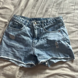 Blå jeansshorts från LAB Industries - Snygga ljusblå jeansshorts i mid Rise från LAB Industries med slitna detaljer och fransig kant. Klassisk femficksmodell med knapp och dragkedja. Perfekta för sommaren och ger en chill vibe till din outfit.