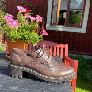 Bruna läderskor med snörning - Snygga bruna läderskor med snörning och dekorativa perforeringar. Skorna har en chunky klack och en robust sula som passar för vardagsbruk. 